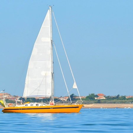 voilier jaune passant devant un phare blanc et rouge au large de l ile de re